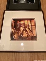 Color photograph showing three glass milk jars with warm amber lighting in a brown wood frame with white matting.