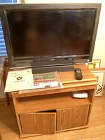 32" Vizio flat screen TV on wooden stand with remote and manual on top.