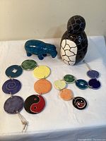 Full view of the ceramic figurines including black and white penguin, teal hippo, and two multicolored round wall hangings laid flat.
