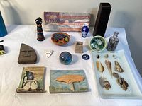 Full lot overview showing most items on white table including vase, beaded doll, plaques, bowls, shells, and granite face slab