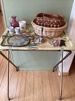 Full view of vintage metal table with all items arranged on top, including baskets, pitcher, bell, egg cups, planter, and wall hangings.
