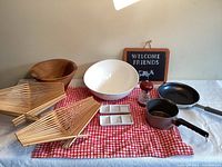 Overview of kitchen items including wooden trays, salad bowls, pans, salt grinder, and condiment dish on red checkered cloth