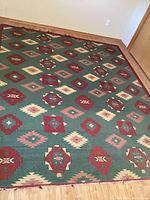 Full view of the woven southwestern motif rug on wood flooring showing general condition and pattern.