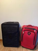 Front view of two suitcases standing side by side: large black Travelpro and smaller red Heys.