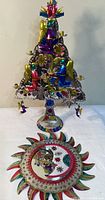 Full view of the colorful Mexican painted tin nativity tree with angels and candle holders on a stand, and the sun-moon decorative mirror on the white background