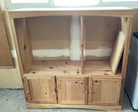 Frontal view of the unfinished pine media cabinet, showing two vertical dividers in shelving and three doors with wooden knobs below.