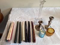 Candles in various colors and sizes, two glass votive holders and three distinct candle holders including sterling or similar metals and acrylic.