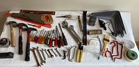 Full view of all tools and hardware laid out on a white surface showing saw, hammers, screwdrivers, wrenches, tape measure, shelf brackets, and other hardware items.