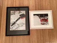 Both photographs framed and laid on a wooden floor, one with a black frame featuring the red and black pen image and the other in a white frame showing a Straus Organic container.