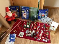 Full overview of all Christmas decorations on red cloth including boxed light-up decorations, stuffed Santa figure, ornaments, and candy cane decorations.