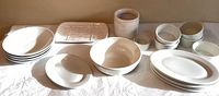 Overview of white dishes including stacked plates, bowls, rectangular platter, ramekins, and Roseville serving bowl arranged on white fabric