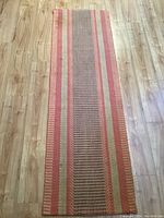 Full view of woven runner rug showing length, red and beige striped pattern, and placement on wooden floor.