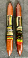 Pair of wooden tapping clamp sticks with pointed ends and decorated with traditional Aboriginal art, showing original labels on each stick.
