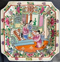 Top-down view of the square porcelain plate showing full hand painted indoor scene with four men, checkerboard floor, floral border, and vivid colors.