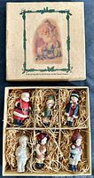 Box with vintage Santa Claus illustration on lid and set of six ornaments packed inside with straw-like material.
