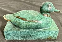 Side angled view of the green patina brass duck figurine on rectangular base showing natural wear and brass accents.