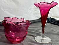 Photo showing both the small ruffled edge cranberry glass vase and the taller stemware cranberry glass vase side by side on a fabric background.