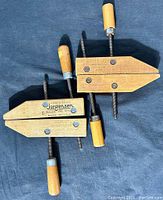 Two wooden Jorgensen clamps placed on a dark fabric background, showing the overall condition and details including wooden handles and metal screws.