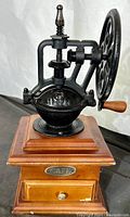 Front view of the vintage manual coffee grinder showing cast iron mechanical components and wooden base with drawer labeled 'CAFE'.