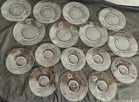 14 clear cut crystal plates arranged in two rows showing etched floral patterns and ringed bases.