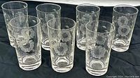 Eight vintage cut crystal tumblers with etched corn flower pattern, arranged together on a black fabric background.