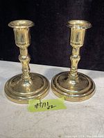 Photo of two solid brass candle holders side by side on a surface with a dark background.