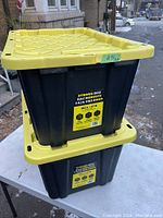 Two stacked black heavy duty storage bins with yellow lids, showing the brand label and general condition.