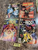 Four vintage Star Trek comics laid out on surface showing front covers with various Star Trek themed art and titles.