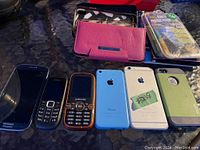 Photo showing multiple phones and cases including Samsung, Nokia, Sony Ericsson models, and Apple iPhones in various colors along with phone cases and screen protector packages.