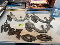 Photo of seven cast iron antique wall mount oil lamp brackets and mounting hardware pieces on a table with books in background