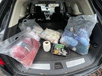 Back of SUV with four large bags of knitting yarn in cream, red and blue colors with a large roll of white thread and a container of sewing accessories in front.