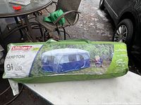 Photo of the tent packed in its green and clear carrying bag showing the Coleman brand, model name Hampton, and tent image.