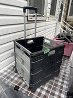 Full view of the folding cart showing black and grey plastic panels, wheels and extended handle.