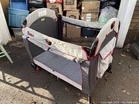 Side view of the Funsport folding bassinet showing fabric, mesh windows, and locking wheels on pavement.