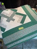 Folded large quilt showing floral and geometric patterns in green, white, and floral fabric.