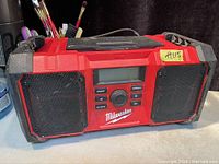 Full front view of the Milwaukee jobsite radio showing speaker grilles, control buttons, and LCD display.