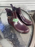 Side perspective of the dark maroon rubber boots showing the buckle strap and pull tab details.
