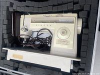 Singer sewing machine inside foam-padded original case, showing machine controls and power cord.