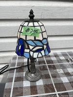 Full view of stained glass lamp showing blue and white floral shade and metal base on checkered surface.
