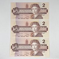 Front side view of the three Canadian $2 bills showing the portrait of Queen Elizabeth II and denomination.