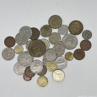 Top-down view of 32 assorted foreign coins spread on a white surface showing various designs and metals.