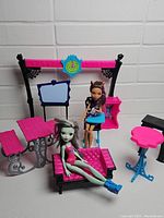 Wide view showing two Monster High dolls and multiple pieces of themed furniture including chaise lounge, desks, table, easel, and shelf unit