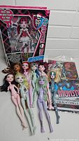 Photo showing nine Monster High dolls without limbs in front of a Fashion Designer set box and unopened tablecover package.