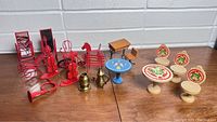 Photo of vintage doll furniture including red metal chairs with mirrors and musical instrument decorations, brass miniatures, wooden table and chair, and floral hand-painted stools and tables