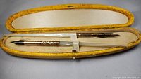 Two antique Victorian dip pens with mother of pearl handles inside a yellow velvet-lined fitted case with secure clasp.