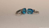 Pair of silver earrings with blue oval stones and small accent stones shown from side angle