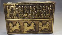 Top view of Egyptian brass box with seven figures in relief artwork and chariots with horses.