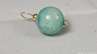 Close-up photo of the spherical green-blue stone pendant with 14K gold loop and bead