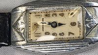 Close-up of the rectangular Art Deco style watch case showing applied gold-tone markers, Johnson branding, and decorative metal frame.
