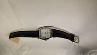 Side angle view of Kenneth Cole rectangular wristwatch with black leather band on light background.
